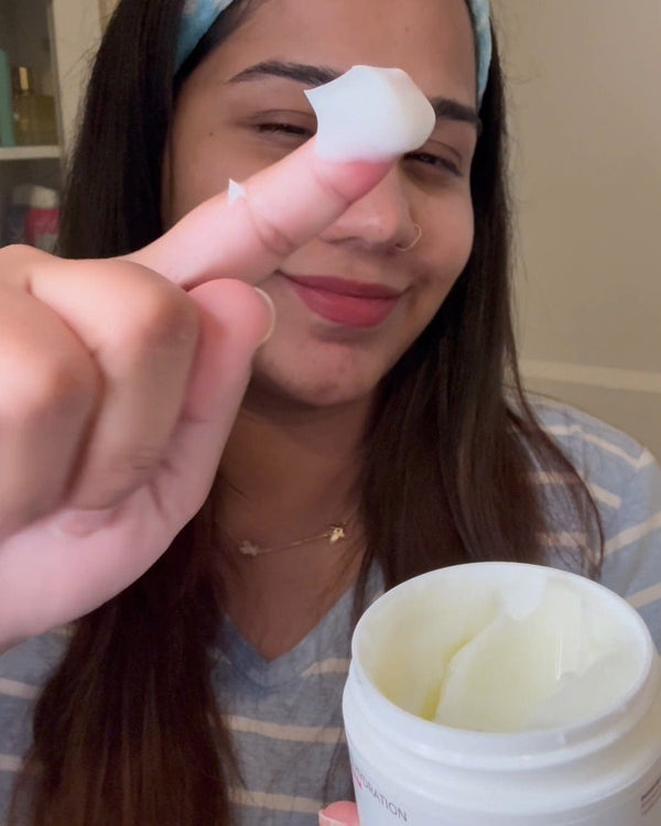 Woman applying cream to her finger with a container of cream in front of her.